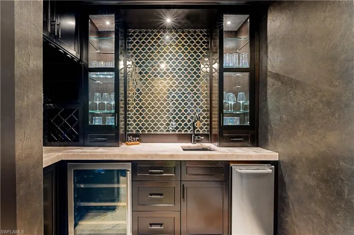 Indoor wet bar featuring beverage cooler, dark brown cabinetry, and light stone countertops