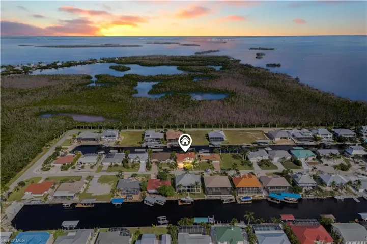 Aerial view showcasing a beautiful home with sweeping water views, nestled in a scenic and well-maintained community. Lush greenery, nearby homes, and tranquil surroundings highlight the perfect blend of nature and neighborhood charm.