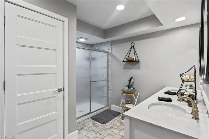 Secondary mater bathroom featuring a shower with shower door, tile patterned flooring, toilet, and dual bowl vanity.