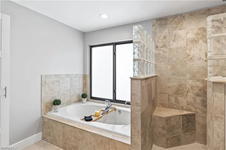 The primary bathroom features a luxurious soaking tub set beneath a large window, offering a serene retreat for relaxing after a long day.