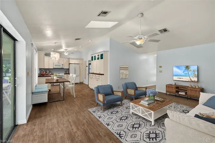 Living room with hardwood / wood-style flooring, lofted ceiling, sink, and ceiling fan with notable chandelier