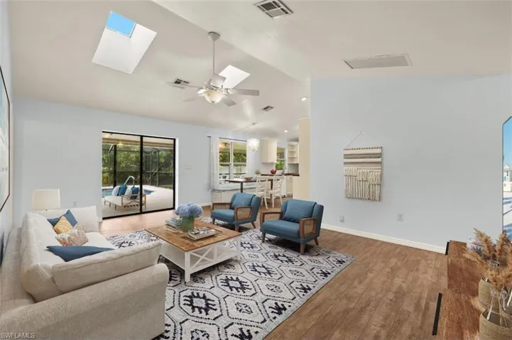 Living room featuring lofted ceiling with skylight, wood-type flooring, and ceiling fan