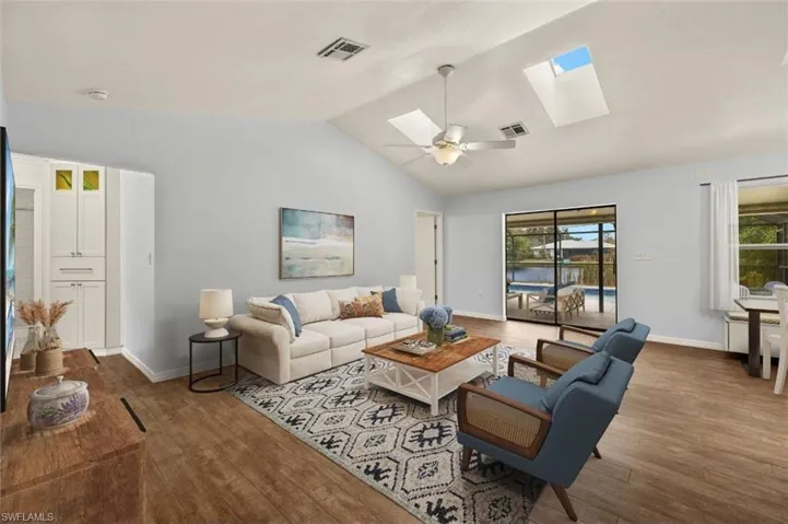 Living room with ceiling fan, wood-type flooring, and vaulted ceiling with skylight