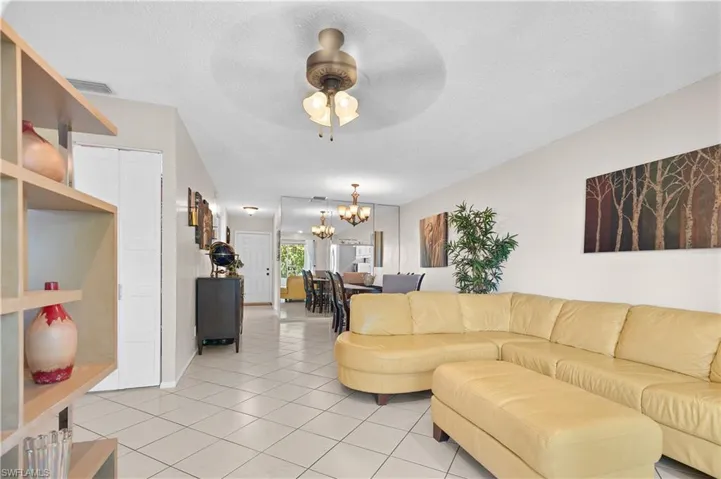 Living room featuring ceiling fan with notable chandelier, a textured ceiling, and light tile floors