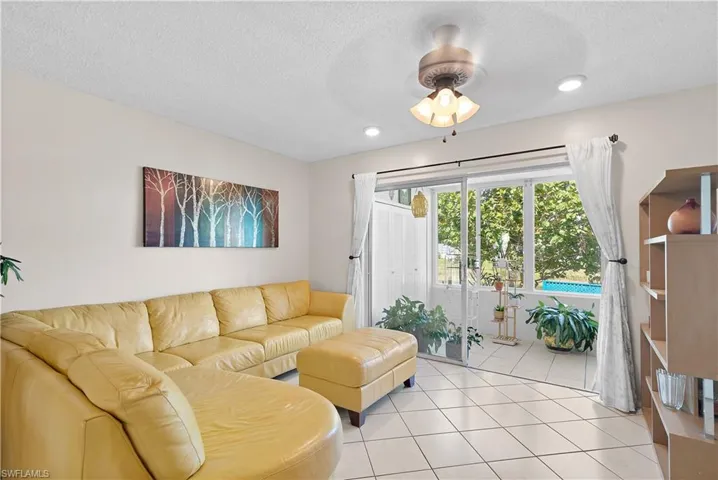 Living room with a textured ceiling, light tile flooring, and ceiling fan