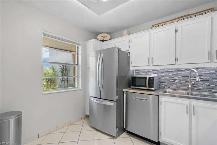 Kitchen featuring stainless steel appliances, backsplash, light tile floors, sink, and white cabinetry