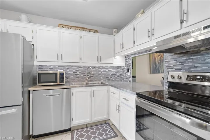 Kitchen featuring backsplash, appliances with stainless steel finishes, sink, and light tile floors
