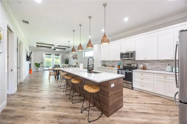 Open-concept kitchen featuring an expansive island with seating, white cabinetry, a tiled backsplash, and stainless steel appliances