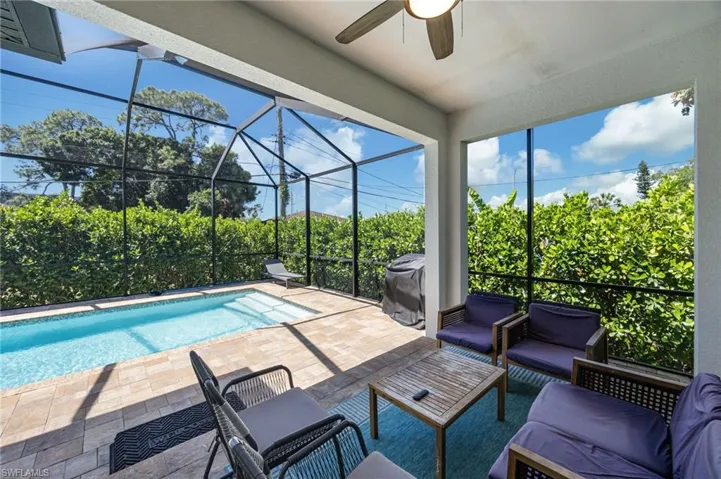 Screened outdoor living area featuring a rectangular pool, paver deck, and mature privacy hedging