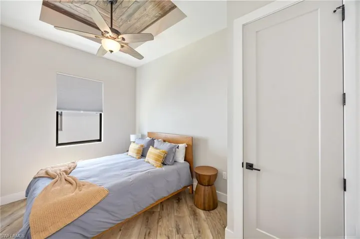 Room featuring wood-finish flooring, a white flat-panel door with matte black hardware, and a window with a roller shade