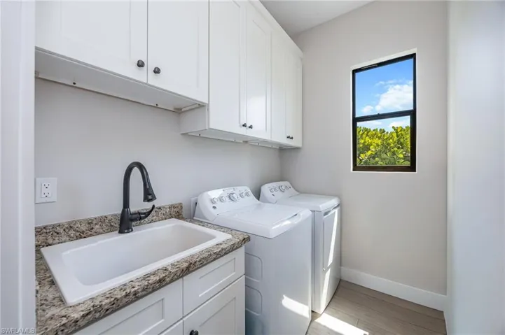Dedicated laundry space featuring white shaker cabinetry, an undermount utility sink with a matte black faucet, granite-finish countertops, and wood-finish flooring