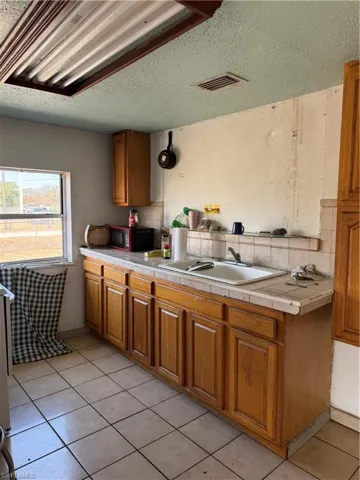 Kitchen featuring wood finish cabinets, tasteful backsplash, light tile patterned floors, a textured ceiling, and tile countertops