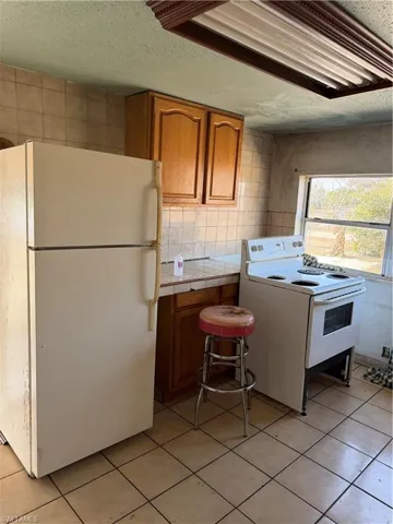 Kitchen featuring tile counters, wood finish cabinetry, refrigerator, a textured ceiling, and light tile patterned flooring