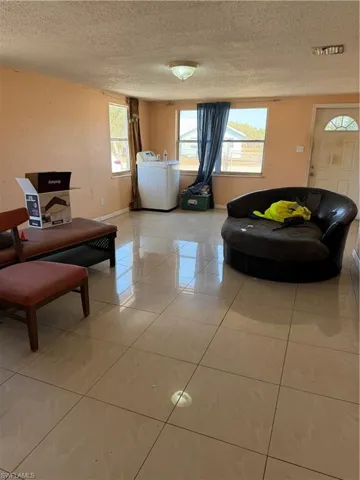 Living room with light tile patterned flooring, a textured ceiling, and washing machine and dryer