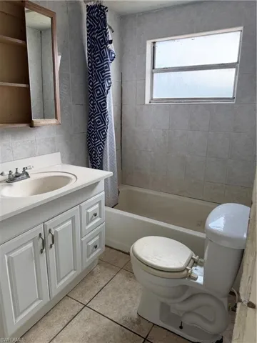 Full bath with vanity, tile walls, shower / bath combo with shower curtain, and light tile patterned floors