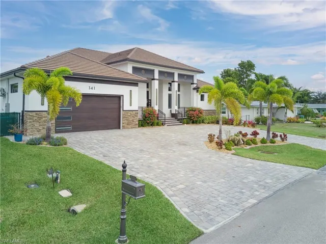 Prairie-style house with stone siding, decorative driveway, a front lawn, stucco siding, and a garage