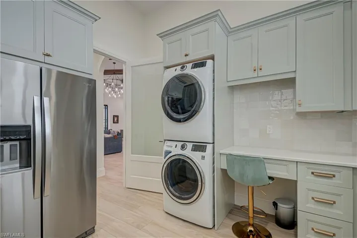 Laundry area with stacked washer and clothes dryer, light wood-type flooring, and a chandelier