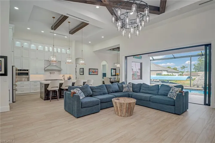 Living area with beamed ceiling, a chandelier, a towering ceiling, light wood-style floors, and arched walkways