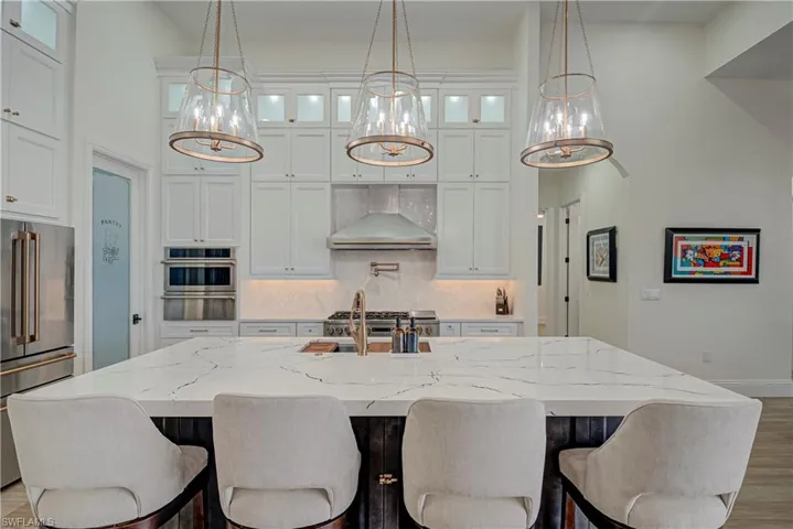 Kitchen featuring glass insert cabinets, white cabinetry, light stone countertops, a high ceiling, and stainless steel appliances