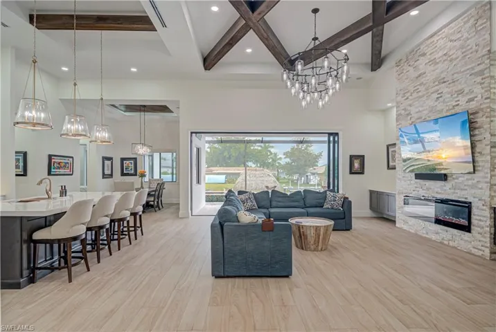 Living room with a chandelier, beam ceiling, a towering ceiling, a stone fireplace, and light wood finished floors