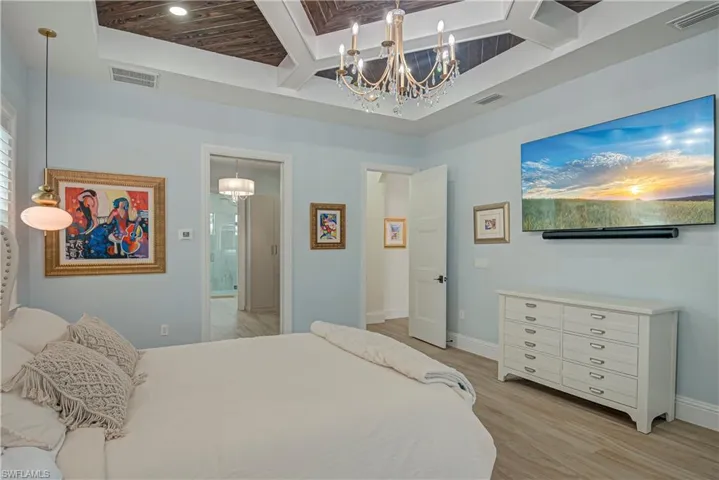 Bedroom featuring a chandelier, coffered ceiling, light wood-style floors, beam ceiling, and a towering ceiling