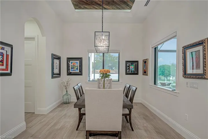 Dining room with light wood-type flooring, a chandelier, a raised ceiling, and arched walkways