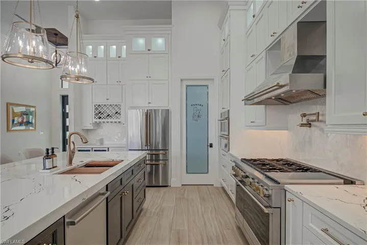 Kitchen with light stone counters, high quality appliances, white cabinets, hanging light fixtures, and a high ceiling