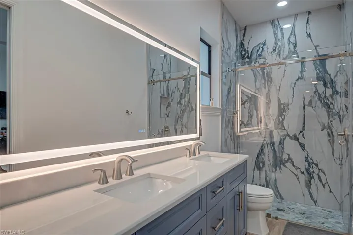 Bathroom featuring double vanity, a marble finish shower, and recessed lighting