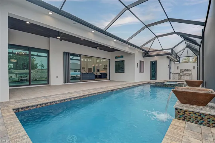 View of pool with glass enclosure, a sunroom, a patio area, and a pool with connected hot tub