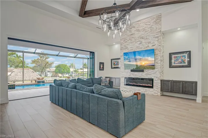 Living room featuring beamed ceiling, light wood finished floors, a high ceiling, a sunroom, and a stone fireplace