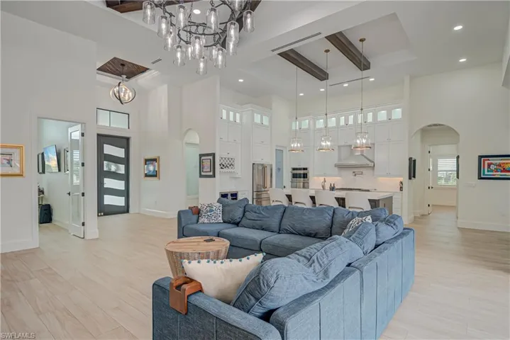 Living area with arched walkways, a chandelier, light wood-style floors, a high ceiling, and beamed ceiling