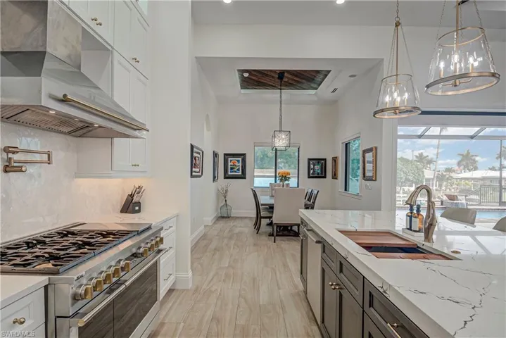 Kitchen featuring double oven range, light stone counters, tasteful backsplash, under cabinet range hood, and hanging light fixtures