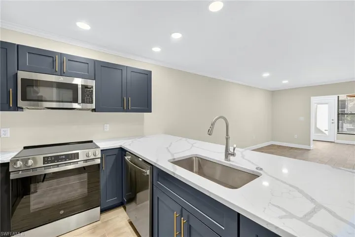 Kitchen with recessed lighting, appliances with stainless steel finishes, light wood-type flooring, crown molding, and light stone countertops