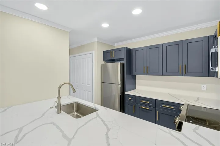 Kitchen featuring light stone counters, ornamental molding, recessed lighting, freestanding refrigerator, and electric range