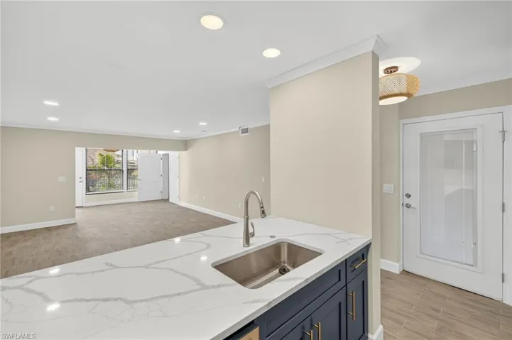 Kitchen featuring wood finish floors, crown molding, recessed lighting, light stone counters, and open floor plan