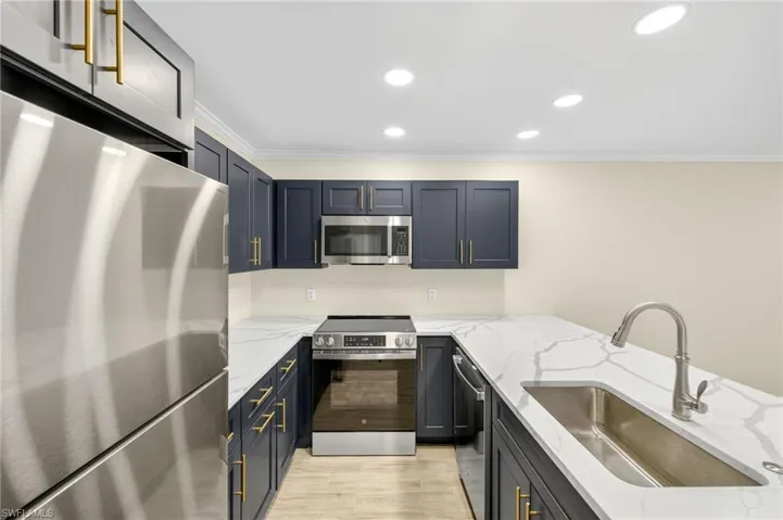 Kitchen with stainless steel appliances, ornamental molding, light stone countertops, recessed lighting, and light wood-style floors