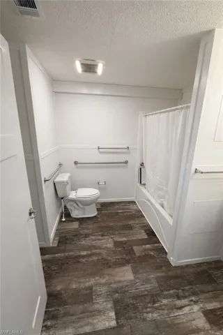 Bathroom featuring wood-finish flooring, a white bathtub with shower, and white walls with wainscoting