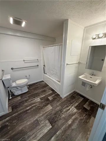Bathroom featuring wood-finish flooring, a wall-mounted sink, a bathtub with shower, and grab bars