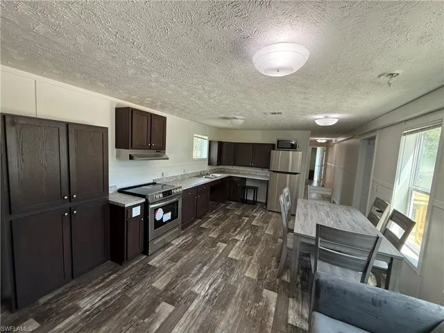 Kitchen featuring dark wood-finish cabinetry, stainless steel appliances, laminate countertops, and wood-look flooring
