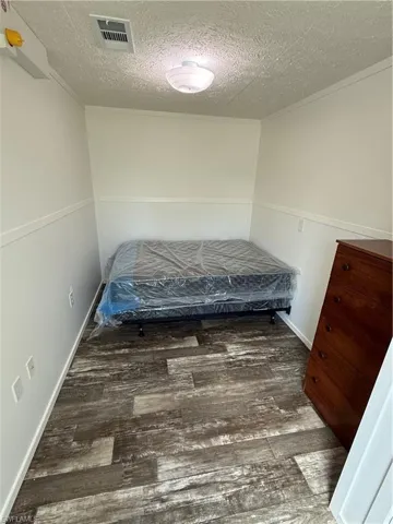 Wood-finish flooring with a textured ceiling, white wall paneling, and an overhead flush-mount light fixture