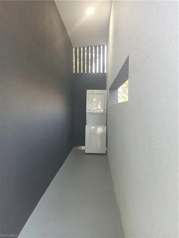 Hallway with a high ceiling, stacked washer and dryer, concrete flooring, and a textured wall