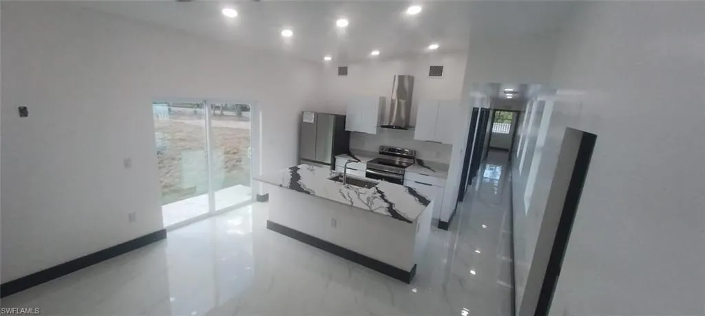 Kitchen featuring sink, stainless steel appliances, light stone countertops, white cabinets, and wall chimney exhaust hood
