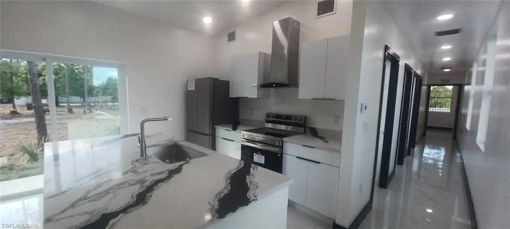 Kitchen featuring stainless steel range with electric cooktop, sink, white cabinets, and wall chimney exhaust hood