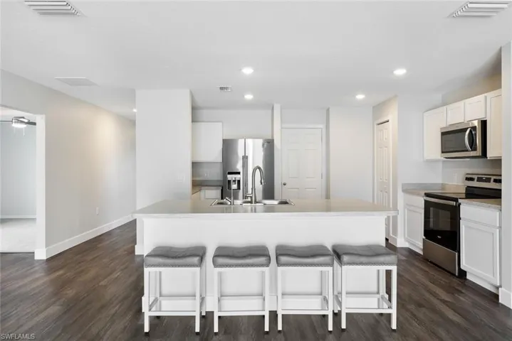 Kitchen featuring dark wood-type flooring, sink, an island with sink, appliances with stainless steel finishes, and white cabinetry