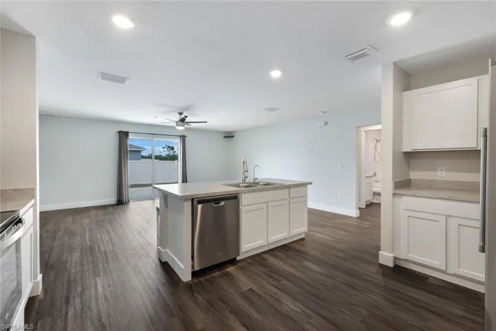 Kitchen with white cabinetry, sink, stainless steel appliances, dark hardwood / wood-style flooring, and a kitchen island with sink
