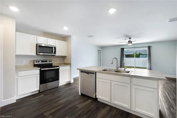 Kitchen featuring white cabinetry, sink, stainless steel appliances, dark hardwood / wood-style floors, and a center island with sink