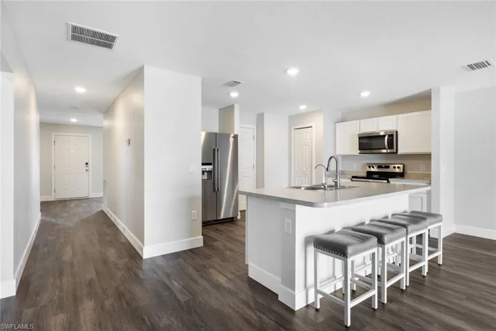 Kitchen featuring a kitchen breakfast bar, dark hardwood / wood-style flooring, stainless steel appliances, white cabinets, and an island with sink
