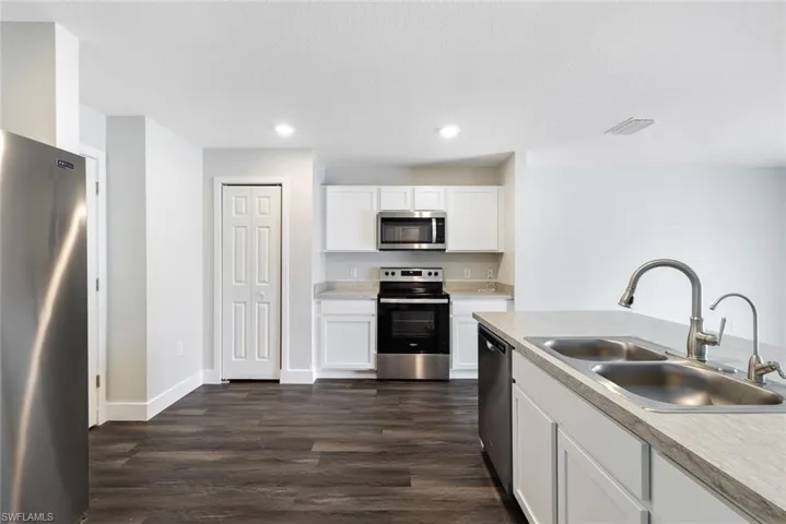 Kitchen featuring dark wood-type flooring, sink, white cabinets, and stainless steel appliances