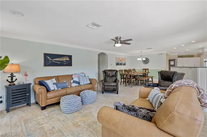 Living room with a ceiling fan, ornamental molding, light wood-style floors, arched walkways, and a chandelier