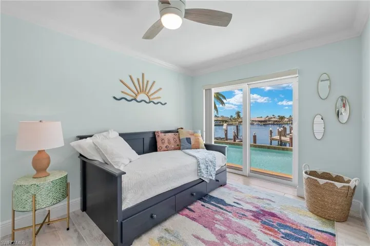 Bedroom with access to outside, a water view, light wood-style flooring, ceiling fan, and ornamental molding